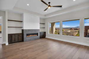 Unfurnished living room featuring a ceiling fan, a fireplace, a mountain view, a tray ceiling, and light wood finished floors