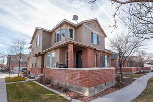 Traditional home featuring brick siding, stucco siding, covered porch, and a front yard
