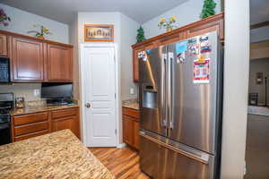 Kitchen with black appliances, light wood-style floors, light stone countertops, and wood finish cabinets