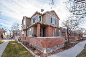 View of front of home featuring brick siding, a front yard, stucco siding, and covered porch