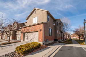 View of side of property with brick siding, concrete driveway, stucco siding, an attached garage, and a residential view