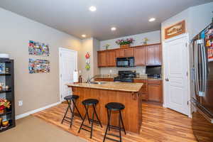Kitchen with wood finish cabinets, a kitchen bar, light stone countertops, black appliances, and a center island with sink
