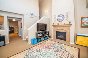 Living area with carpet, a high ceiling, and a glass covered fireplace