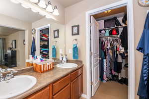 Bathroom featuring a spacious closet, double vanity, and light carpet