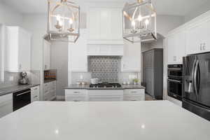 Kitchen featuring black appliances, white cabinetry, hanging lights, dark stone counters, and backsplash