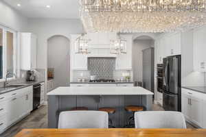Two tone kitchen with stainless steel appliances, arched walkways, a chandelier, a kitchen island, and dark stone countertops