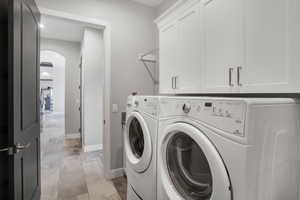 Laundry area featuring arched walkways, cabinet space, and washing machine and dryer