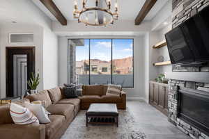 Living room featuring beamed ceiling, a stone fireplace, hanging lights, and light wood-style floors