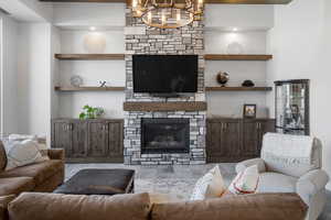 Living area featuring a stone fireplace, a chandelier, and built in shelves