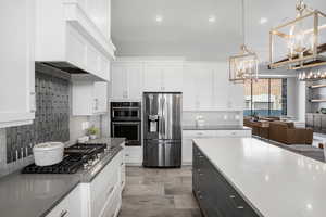 Two tone kitchen with stainless steel appliances, backsplash, dual tone cabinets, dark stone counters, and open floor plan