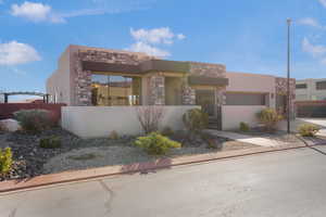 Pueblo-style house with stone siding, a fenced front yard, stucco siding, a gate, and driveway