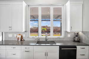 Kitchen with black dishwasher, white cabinets, dark stone countertops, and decorative backsplash