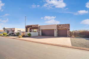 Pueblo-style house featuring stone siding, concrete driveway, stucco siding, and a garage