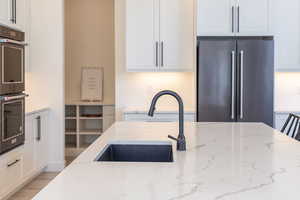 Kitchen featuring white cabinetry, high quality fridge, double wall oven, light stone countertops, and wood finished floors