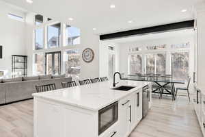 Kitchen with light stone counters, a center island with sink, a kitchen bar, white cabinets, and stainless steel appliances