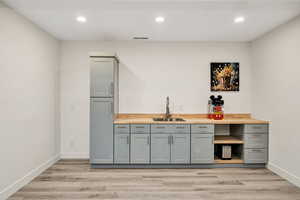 Indoor wet bar featuring gray cabinetry, recessed lighting, butcher block countertops, and light wood finished floors