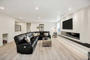 Living room with recessed lighting, a glass covered fireplace, and light wood-type flooring
