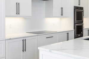 Kitchen with light stone counters, white cabinetry, and black appliances