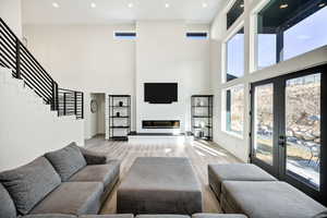 Living room with light wood-style floors, a glass covered fireplace, recessed lighting, a high ceiling, and french doors