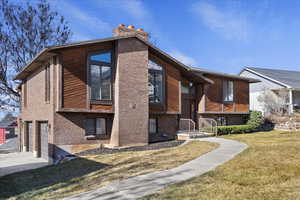 View of home's exterior featuring an attached garage, a yard, a chimney, brick siding, and driveway