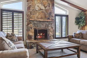 Carpeted living area featuring vaulted ceiling with beams and a fireplace