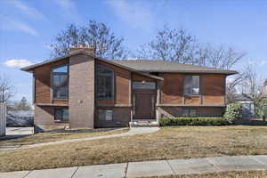 Raised ranch with a chimney, a front lawn, brick siding, and roof with shingles