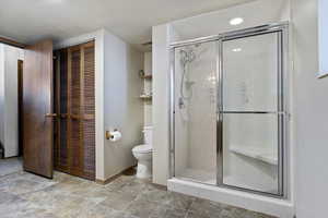 Full bath featuring a closet, a stall shower, and stone finish floors