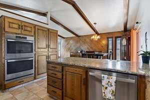 Kitchen with stainless steel appliances, wooden walls, wood finish cabinetry, beamed ceiling, and a chandelier
