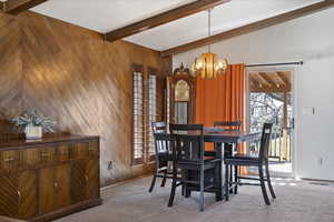 Dining space featuring light colored carpet, wood walls, hanging lights, and beam ceiling