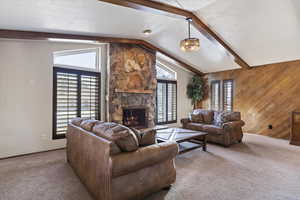Living room featuring carpet, beamed ceiling, wood walls, a fireplace, and a textured ceiling