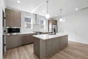 Photo of finished unit - Kitchen featuring modern cabinets, light wood finished floors, tasteful backsplash, stainless steel appliances, and pendant lighting