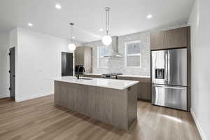 Photo of finished unit - Kitchen with stainless steel appliances, modern cabinets, decorative light fixtures, light stone countertops, and light wood-style floors