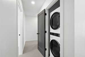 Photo of finished unit - Laundry area featuring stacked washer and clothes dryer and light colored carpet