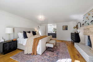 Bedroom with wood-type flooring, ensuite bath, ornamental molding, and a fireplace