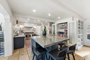 Kitchen featuring range with two ovens, light stone counters, a breakfast bar area, stone tile flooring, and tasteful backsplash