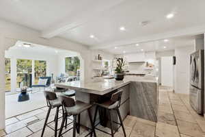 Two tone kitchen with stone tile flooring, a breakfast bar area, freestanding refrigerator, open shelves, and light stone counters