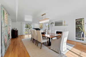 Dining area featuring light wood-style floors and a warm lit fireplace