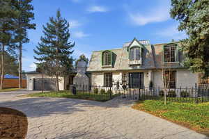 View of property featuring a fenced front yard, mansard roof, driveway, a high end roof, and a garage