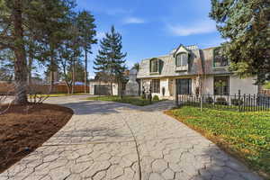 View of front of home with mansard roof, a high end roof, curved driveway, and a fenced front yard