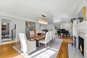 Dining area featuring ornamental molding, light wood-type flooring, a fireplace, and suspended lighting