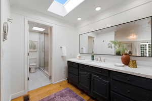 Bathroom featuring a skylight, vanity, a shower stall, light wood-type flooring, and crown molding
