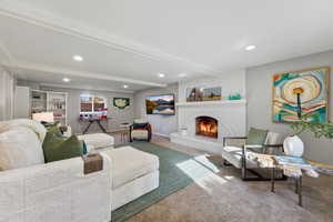 Carpeted living room with beam ceiling, recessed lighting, and a brick fireplace