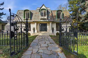 View of front facade with mansard roof, a fenced front yard, brick siding, a high end roof, and a gate