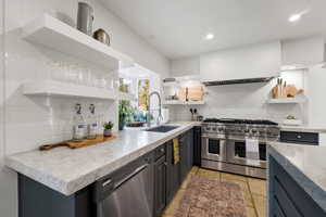 Kitchen with open shelves, stainless steel appliances, light stone counters, stone tile flooring, and recessed lighting