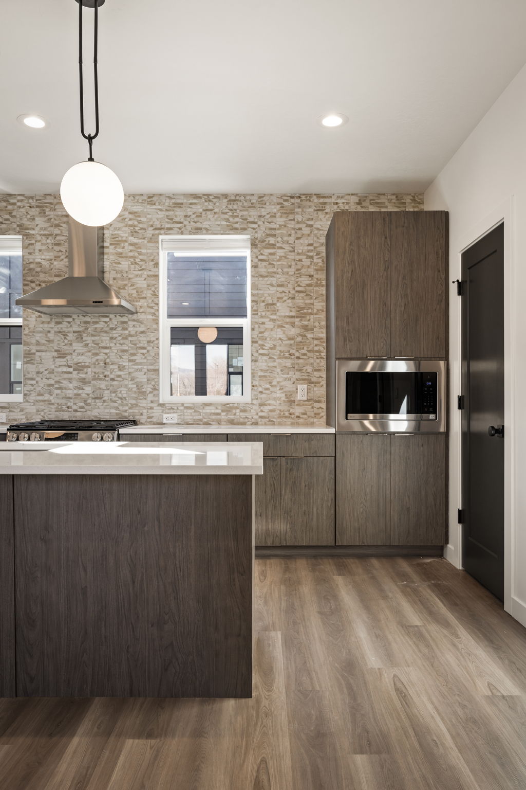 Kitchen with dark wood-style floors, pendant lighting, stainless steel microwave, modern cabinets, and backsplash
