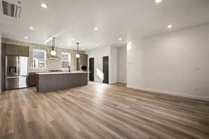 Kitchen with open floor plan, a center island with sink, cooling unit, hanging light fixtures, and stainless steel fridge