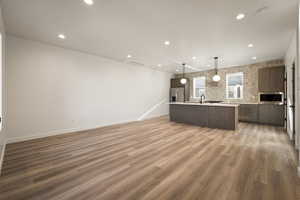 Kitchen with open floor plan, decorative light fixtures, a kitchen island with sink, light wood finished floors, and modern cabinets
