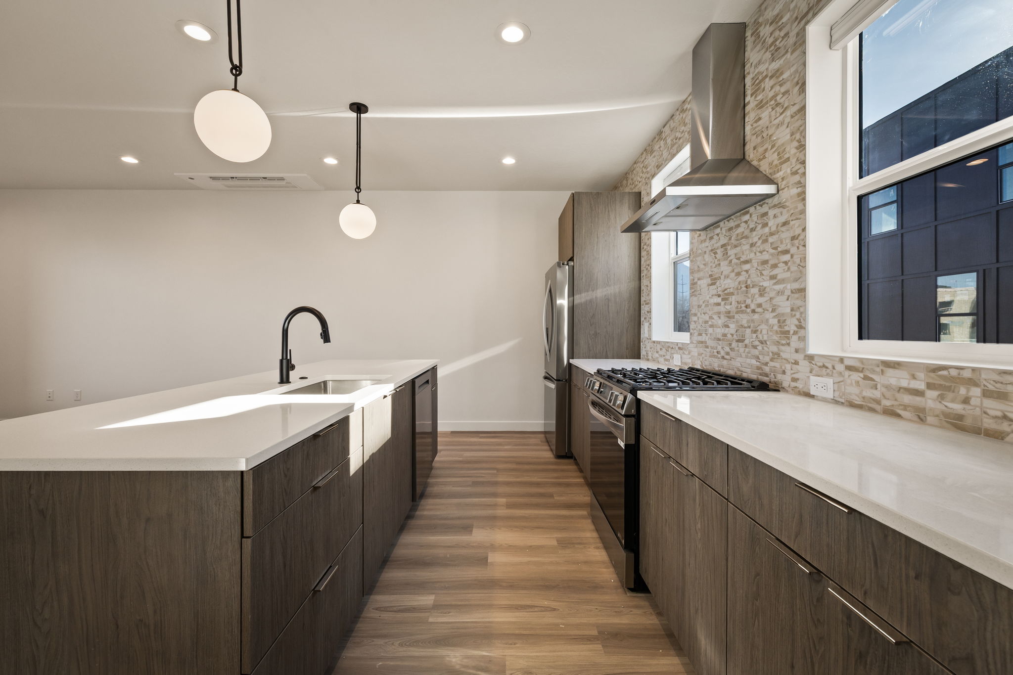 Kitchen featuring modern cabinets, stainless steel appliances, backsplash, hanging light fixtures, and dark wood finished floors