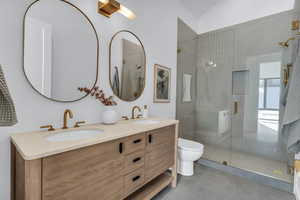 Bathroom featuring double vanity, a stall shower, lofted ceiling, and light tile patterned floors