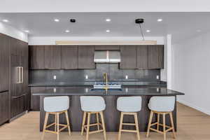Kitchen with a kitchen bar, light wood-style flooring, a center island with sink, and backsplash